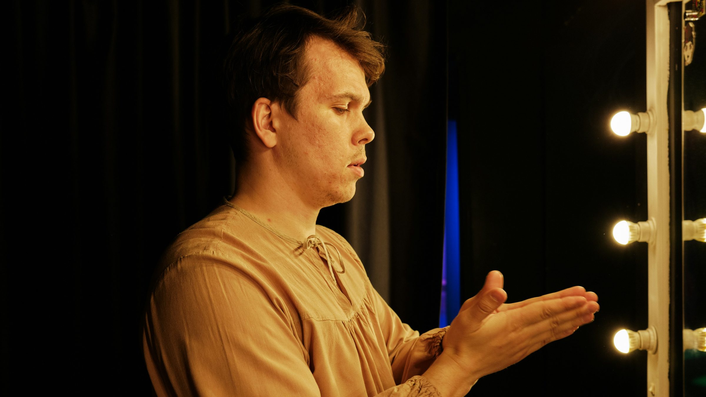 A performer waiting by dressing room mirror lights